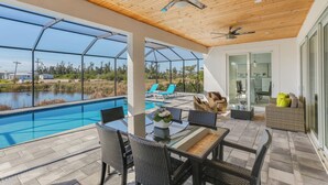 A poolside area with a glass enclosure, outdoor furniture, and a ceiling fan.