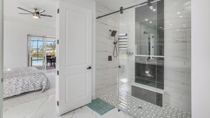 A modern bathroom with a glass-enclosed shower, a ceiling fan, and a view of an outdoor pool.