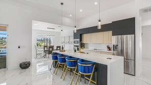 A modern kitchen with a white island, stainless steel appliances, and blue bar stools.
