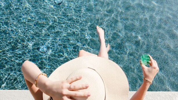 Eine Person entspannt am Pool, mit einem Hut, auf dem 'Hello Sunshine' steht.