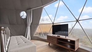 Ein modernes Zimmer mit großem Fenster, einer Couch, einem Holz-Fernsehschrank und einem Vorhang.