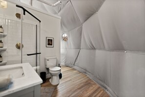 Une salle de bain moderne avec un mur recouvert de carreaux blancs, des toilettes blanches et un lavabo doté d’un plan de travail en marbre.