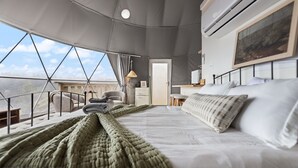 Ein gemütlicher, runder Raum mit einem großen Bett, einem Schreibtisch und einem Sessel. Das Zimmer verfügt über ein großes Fenster mit weitreichendem Ausblick.