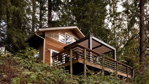 A cabin with a wooden exterior, a balcony, and surrounded by dense forest.