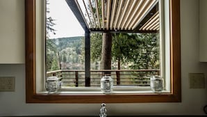 A kitchen with a window overlooking a balcony and a view of trees and a lake.