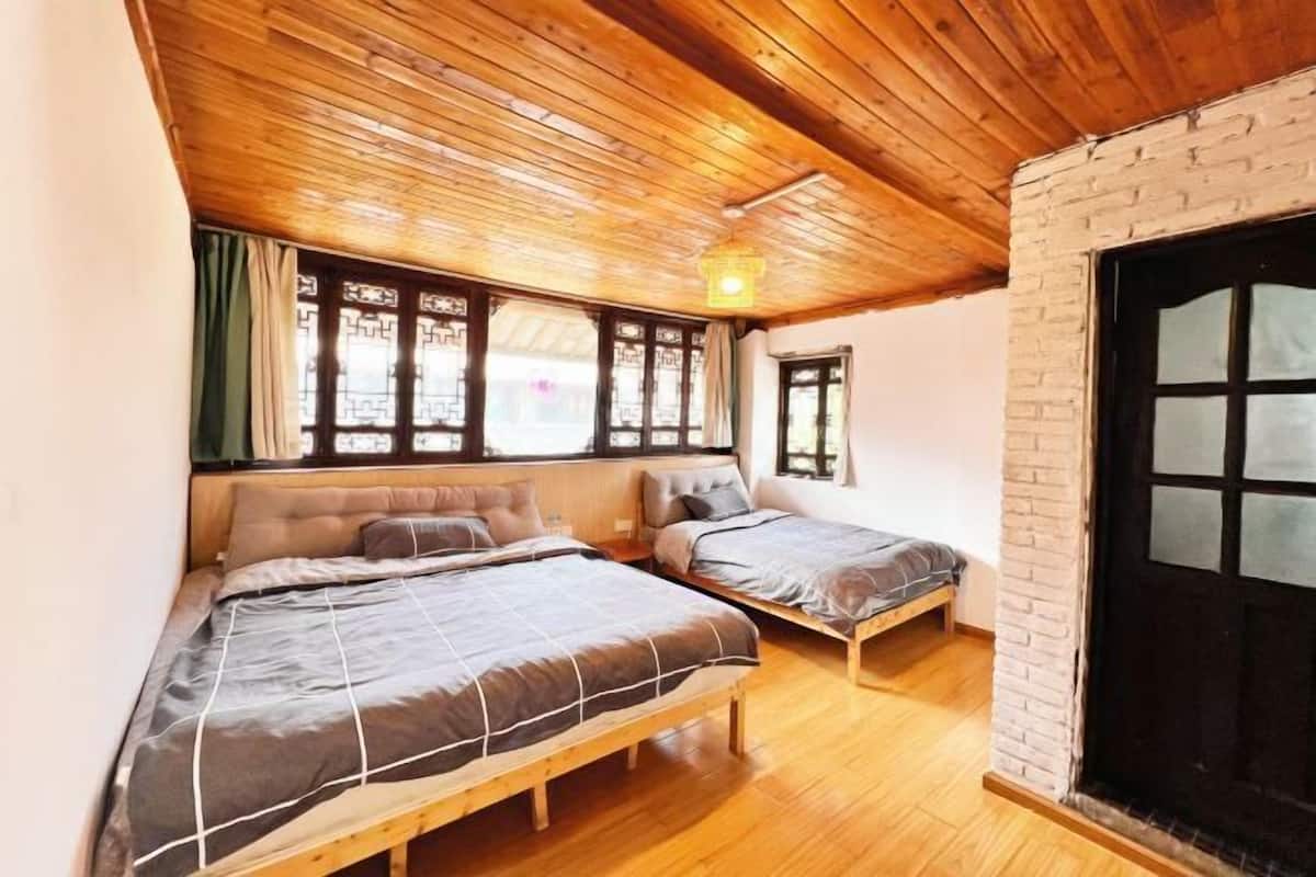 A room with two beds, wooden ceiling, and a brick wall.