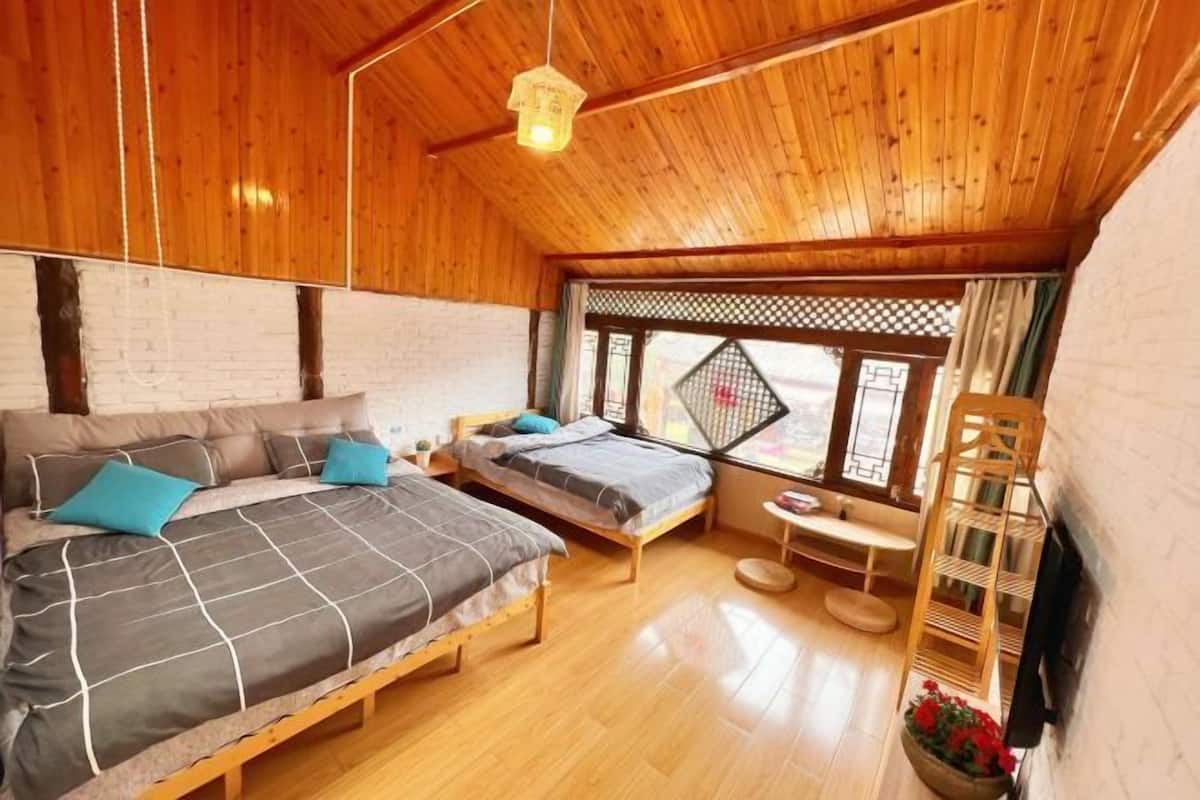 A wooden cabin with two beds, a small table, a chair, and a window with a view.