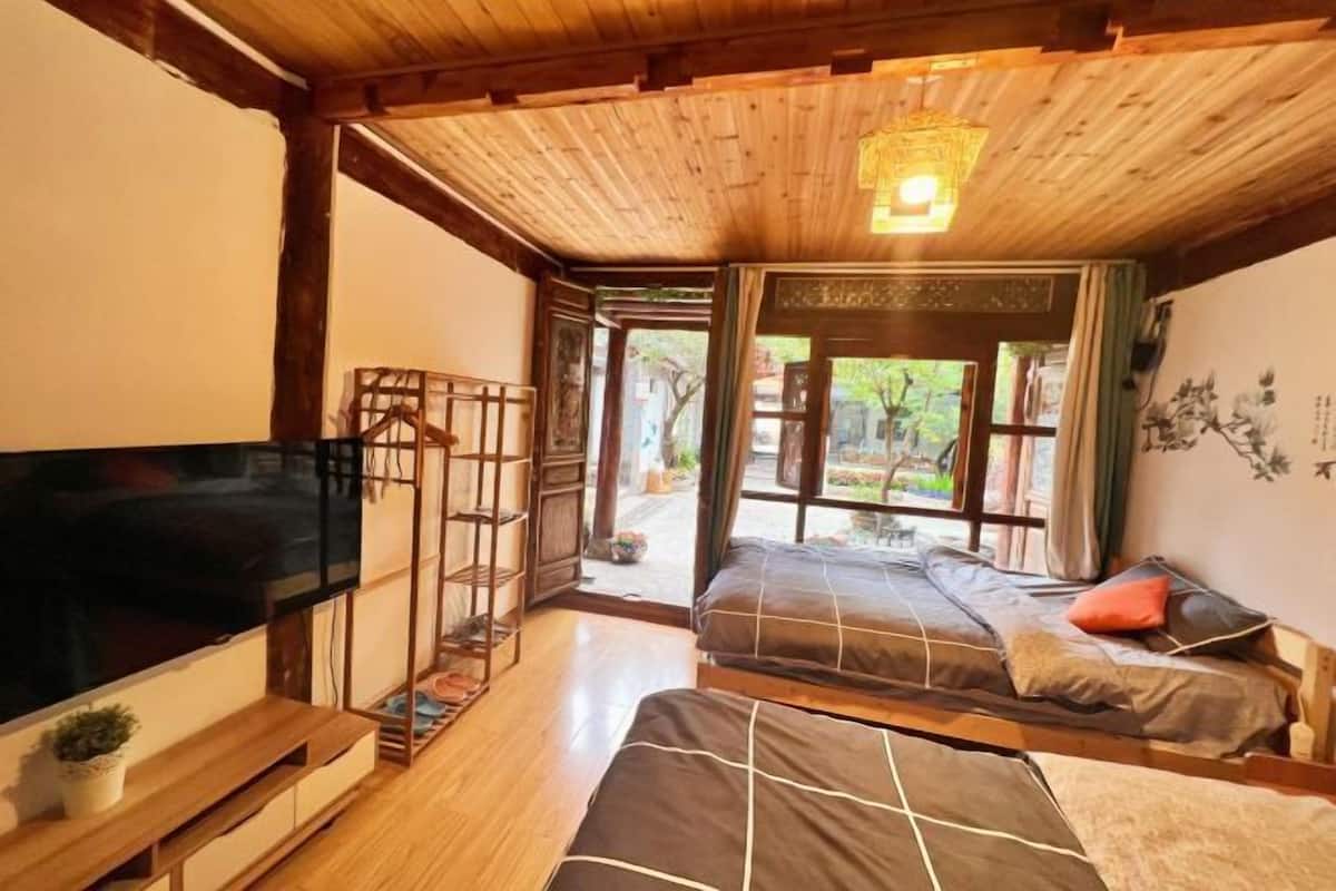 A room with a TV, two beds, a wooden ceiling, and a view of the outdoors.