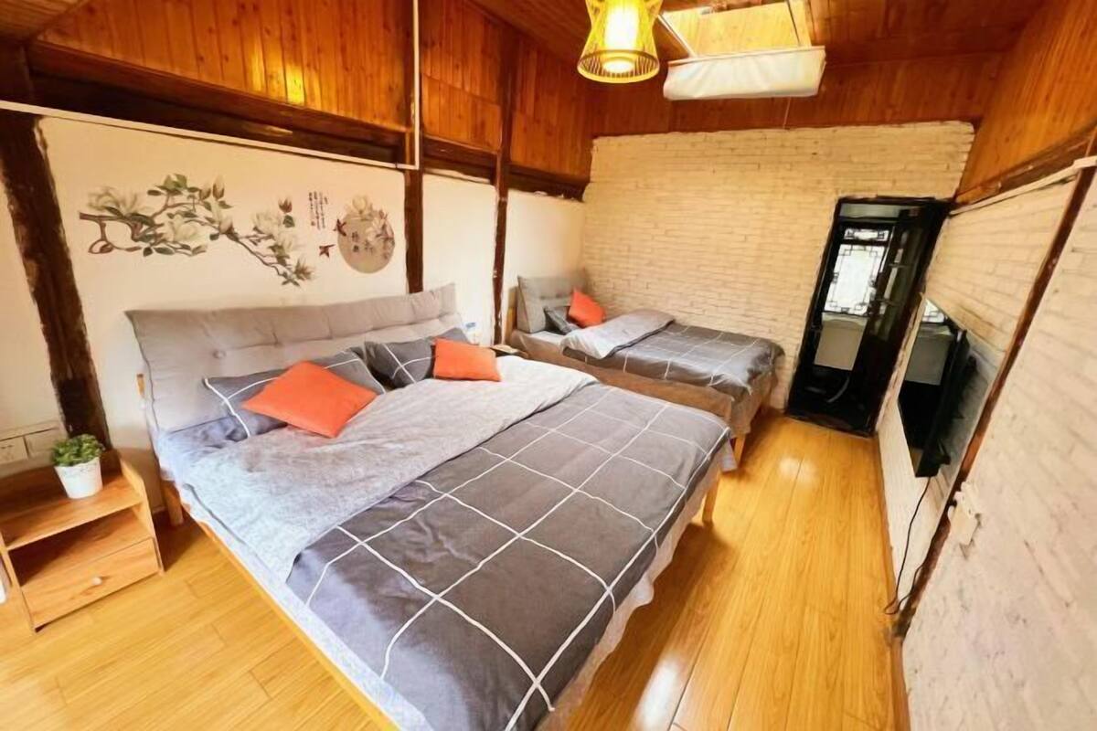 A cozy room with a large bed, two smaller beds, wooden flooring, a brick wall, and a television.