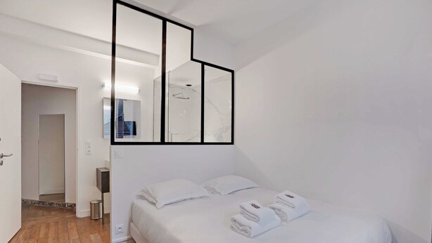 A hotel room with a large bed, white linens, a mirror with black frames, and a wooden floor. - Duplex Loft Montmartre -18th (Paris)