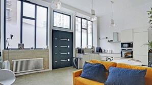 A modern kitchen with white cabinets, a microwave, and a coffee machine. There is a black door and a radiator. - Duplex Loft Montmartre -18th (Paris)