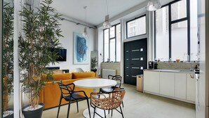A modern kitchen with white cabinets, a black door, and a dining area with a round table and chairs. - Duplex Loft Montmartre -18th (Paris)