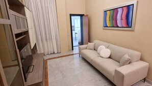 A living room with a beige sofa, a framed abstract painting, and a wooden cabinet. - Paradise Inn 2 (Livorno)