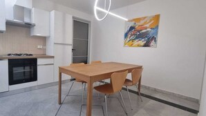 A modern kitchen with white cabinets, a gas stove, and a dining table with chairs. - Paradise Inn 2 (Livorno)