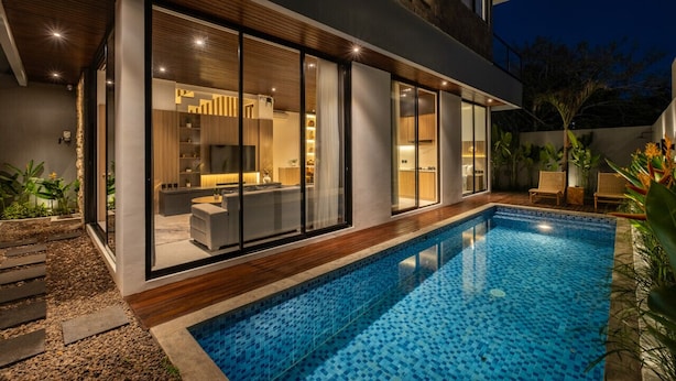 A modern house with a swimming pool, large glass windows, and a well-lit interior.