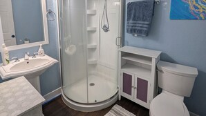 Un baño con cabina de ducha de vidrio, un lavabo blanco, un inodoro y una pared azul.