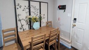 Un comedor con una mesa y sillas de madera, un adorno en la pared y una puerta blanca con buzón.