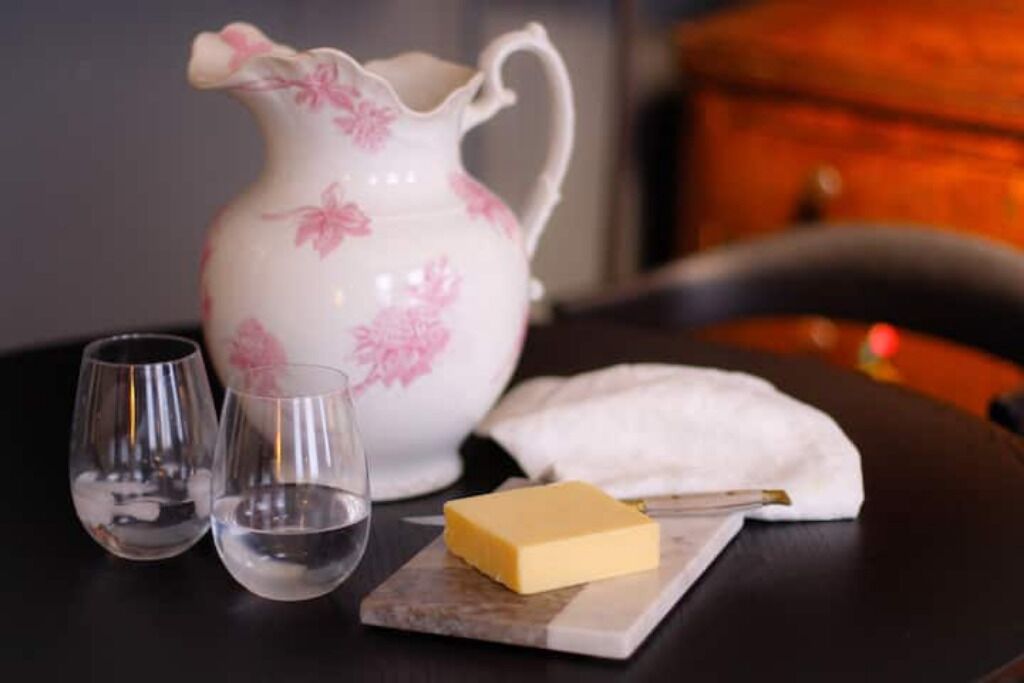 A table with a pitcher, two glasses, a block of butter, and a napkin.