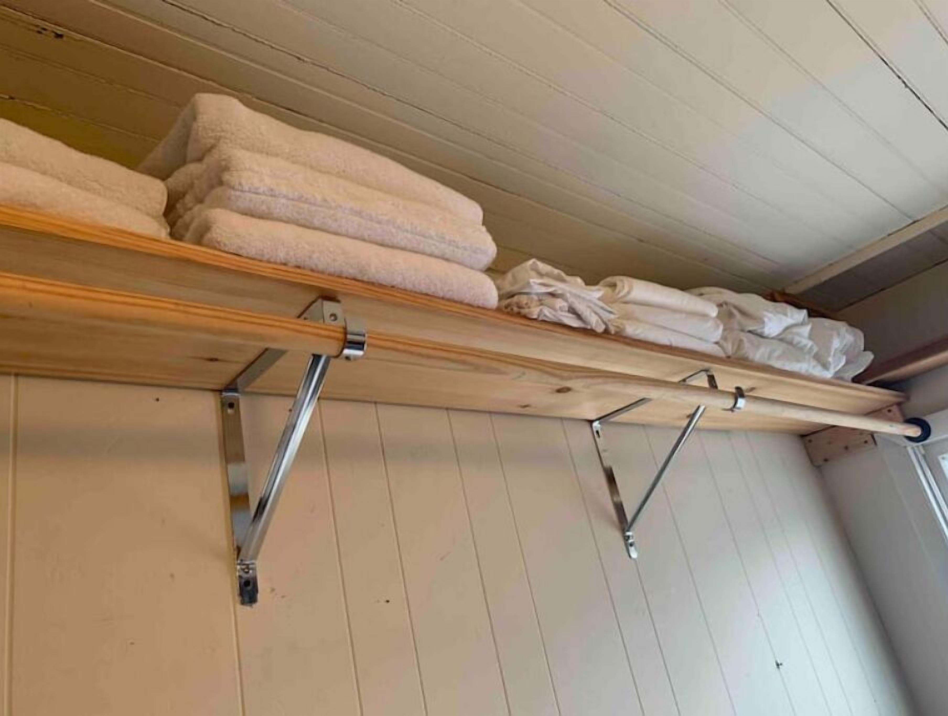 A wooden shelf with folded towels and a drying rack against a wooden wall.