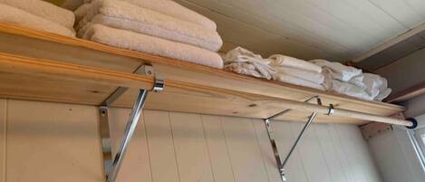 A wooden shelf with folded towels and a drying rack against a wooden wall.