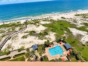 A beach resort with a swimming pool, beach umbrellas, and a boardwalk.