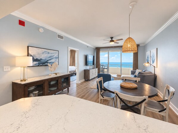 A modern living room with a large window, a ceiling fan, and a dining area with a marble table.