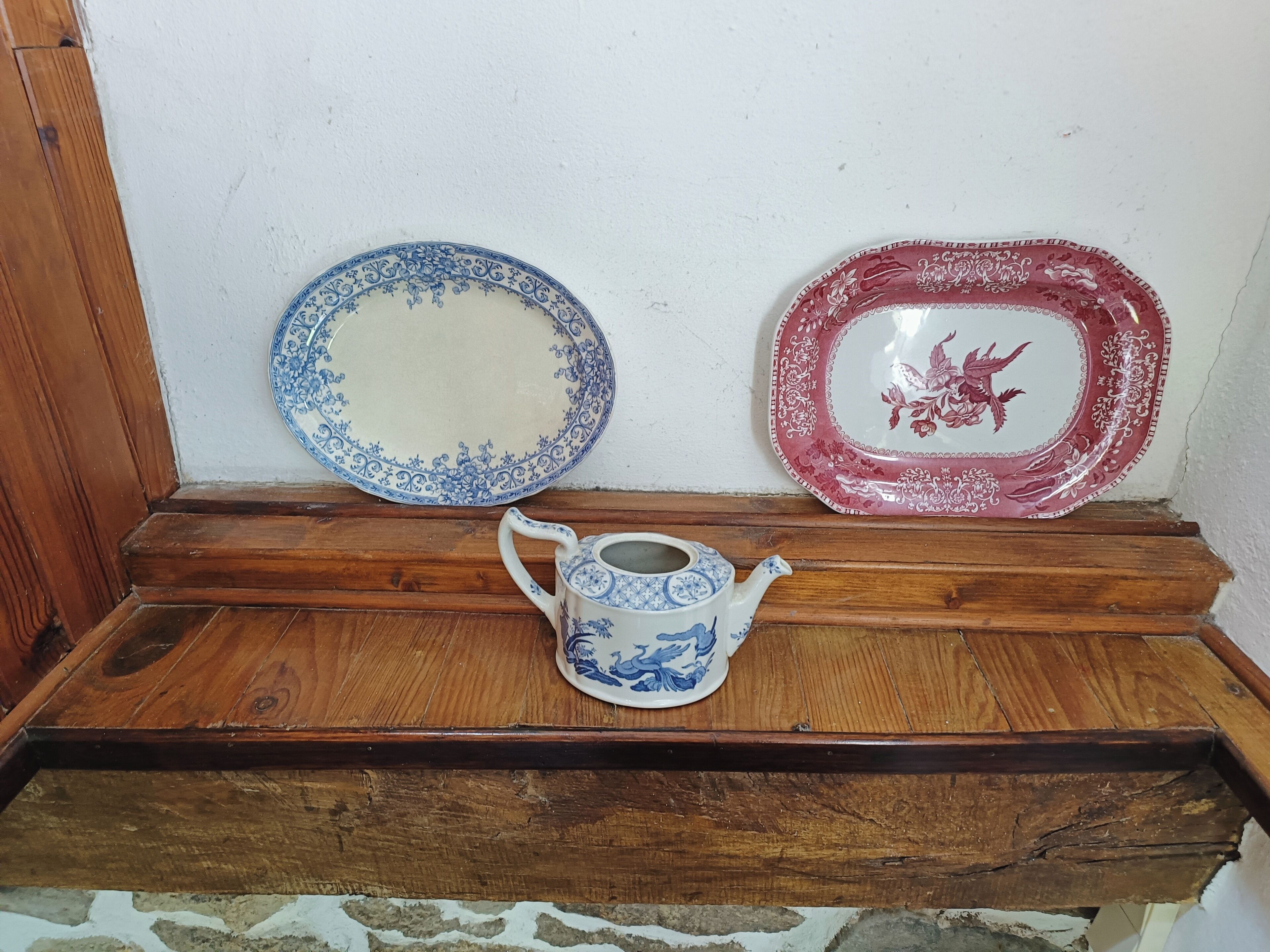 A wooden shelf with two ceramic plates and a teapot.