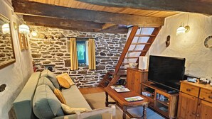 Un salon chaleureux avec un mur en pierre, un plafond en bois, un canapé, un téléviseur et un meuble en bois.