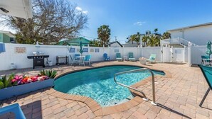 Un área de piscina con una piscina azul cristalina, sillas de descanso y una parrilla.