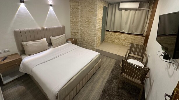 Quarto com cama, mesa de cabeceira e um pequeno espaço de estar com cadeiras.