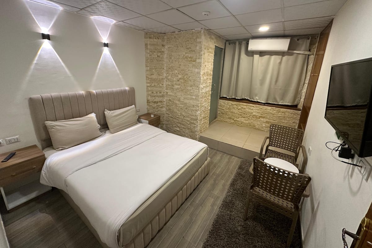 Un dormitorio con cama, mesita de noche y una pequeña zona de estar con sillones.