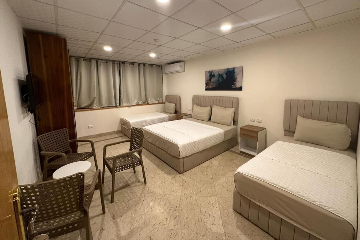 Habitación de hotel con dos camas, un escritorio, una silla, una mesita y una ventana con cortinas.