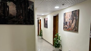 Um corredor com piso de azulejos, um grande quadro clássico à esquerda e outro à direita.