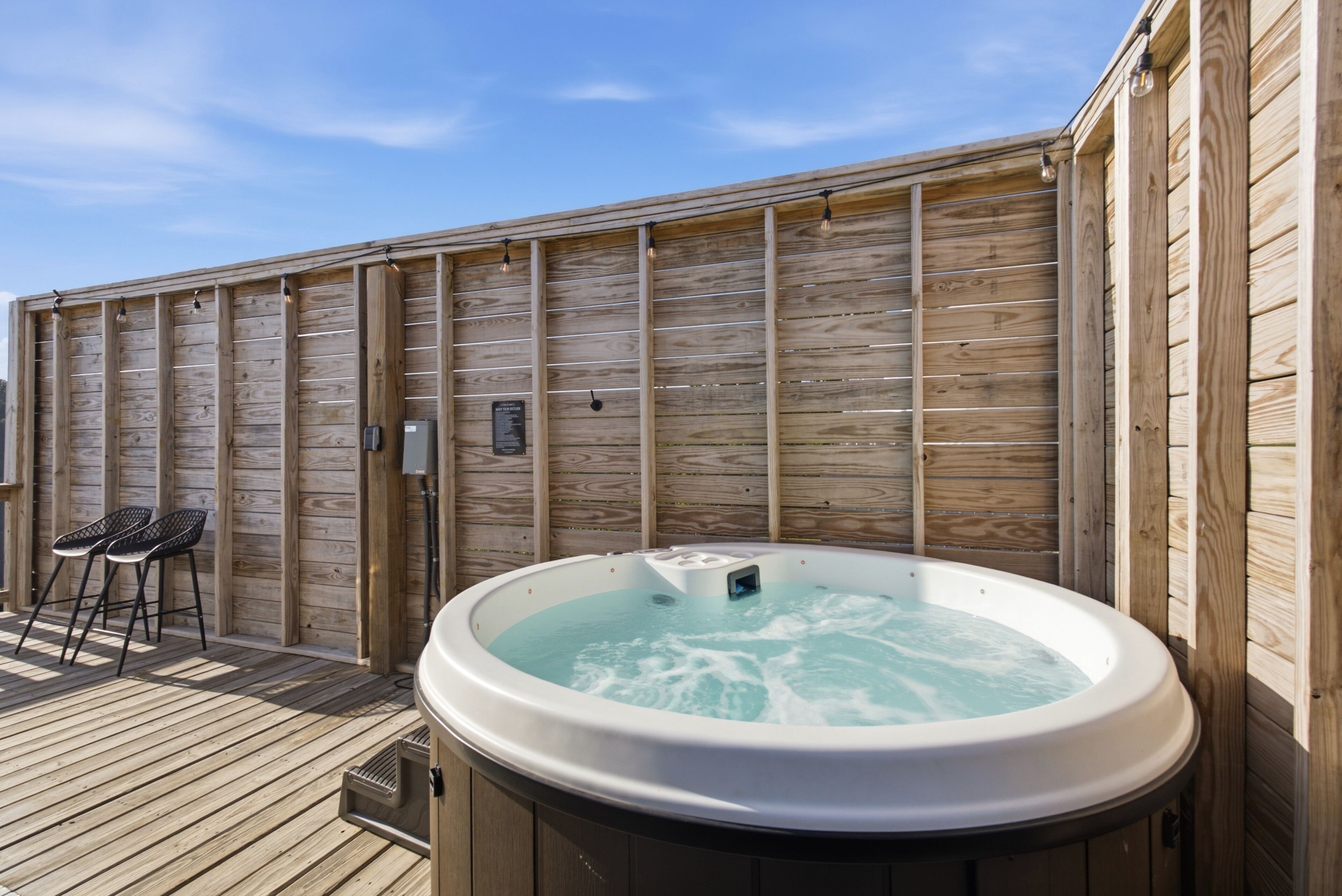 A wooden deck with a hot tub, two bar stools, and a wooden wall with a sign.