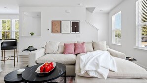 A modern living room with a sectional sofa, a coffee table with apples, and a dining area with a black chair and table.