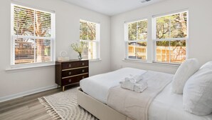 A bedroom with a bed, a dresser, and two windows with blinds.