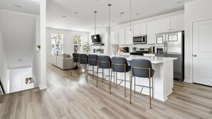 Una cocina moderna con armarios blancos, electrodomésticos de acero inoxidable y una barra con cuatro taburetes.