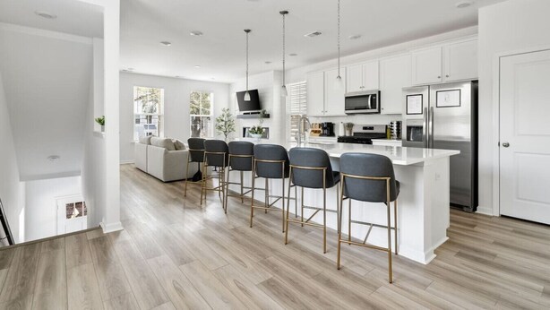 A modern kitchen with white cabinets, stainless steel appliances, and a bar area with four stools.