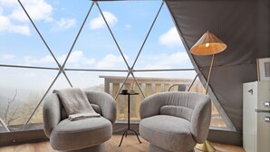 A modern room with two grey armchairs, a floor lamp, and a view of the outdoors through a large window. - Hot Tub Dome with Epic Ridge Views- Hickory Heights (Stanton)