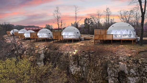 A row of dome-shaped yurts with wooden benches and tables, set against a backdrop of trees and a sunset sky. - Hot Tub Dome with Epic Ridge Views- Hickory Heights (Stanton)