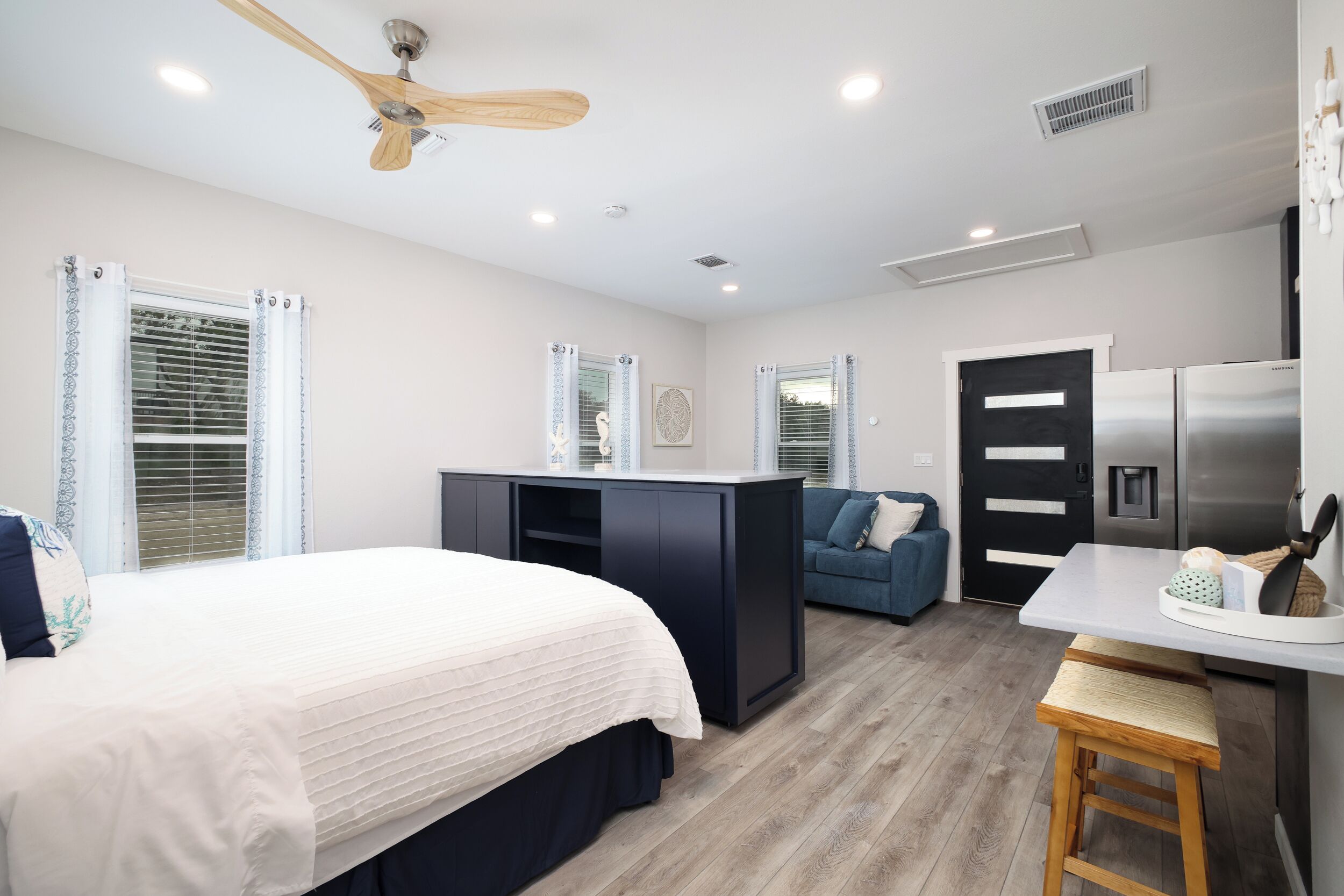 A modern bedroom with a bed, a desk, a kitchenette, and a ceiling fan.