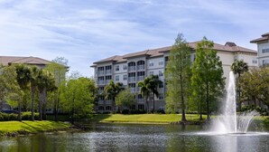 Un hotel con una fuente de agua, rodeado de vegetación y un lago.