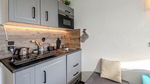 Cozinha compacta com armários cinza, forno preto e painel atrás do fogão em madeira.