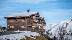 Uma chalé de madeira com varandas, com vista para uma montanha coberta de neve.