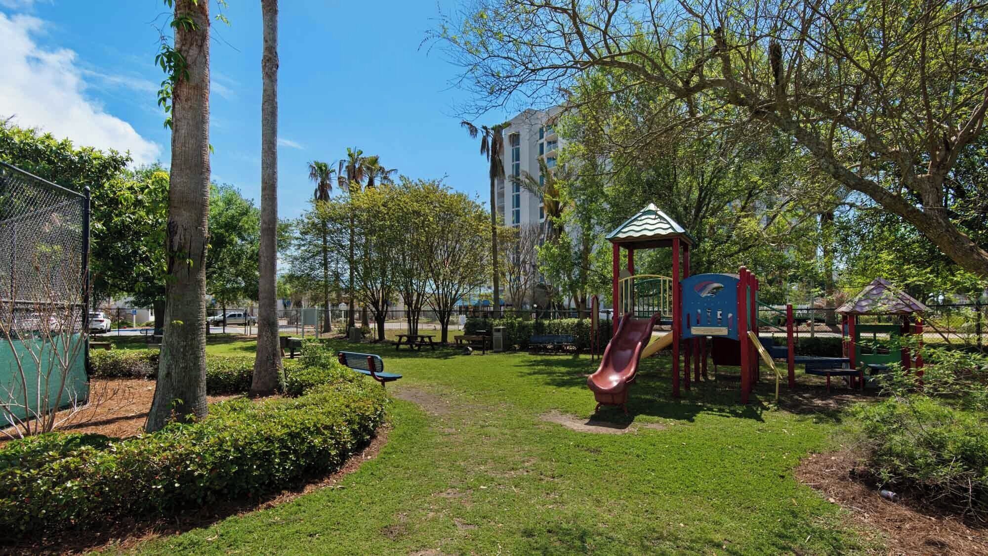 A park with a playground, benches, and a clear sky.