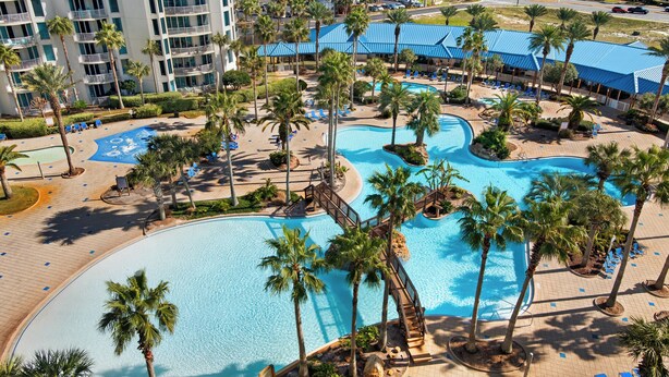 A resort with multiple swimming pools, palm trees, and a large building with balconies. - Palms Resort 2813: 2br, Pools, Courts, Gulf Views & Minutes to Beach! (Destin)
