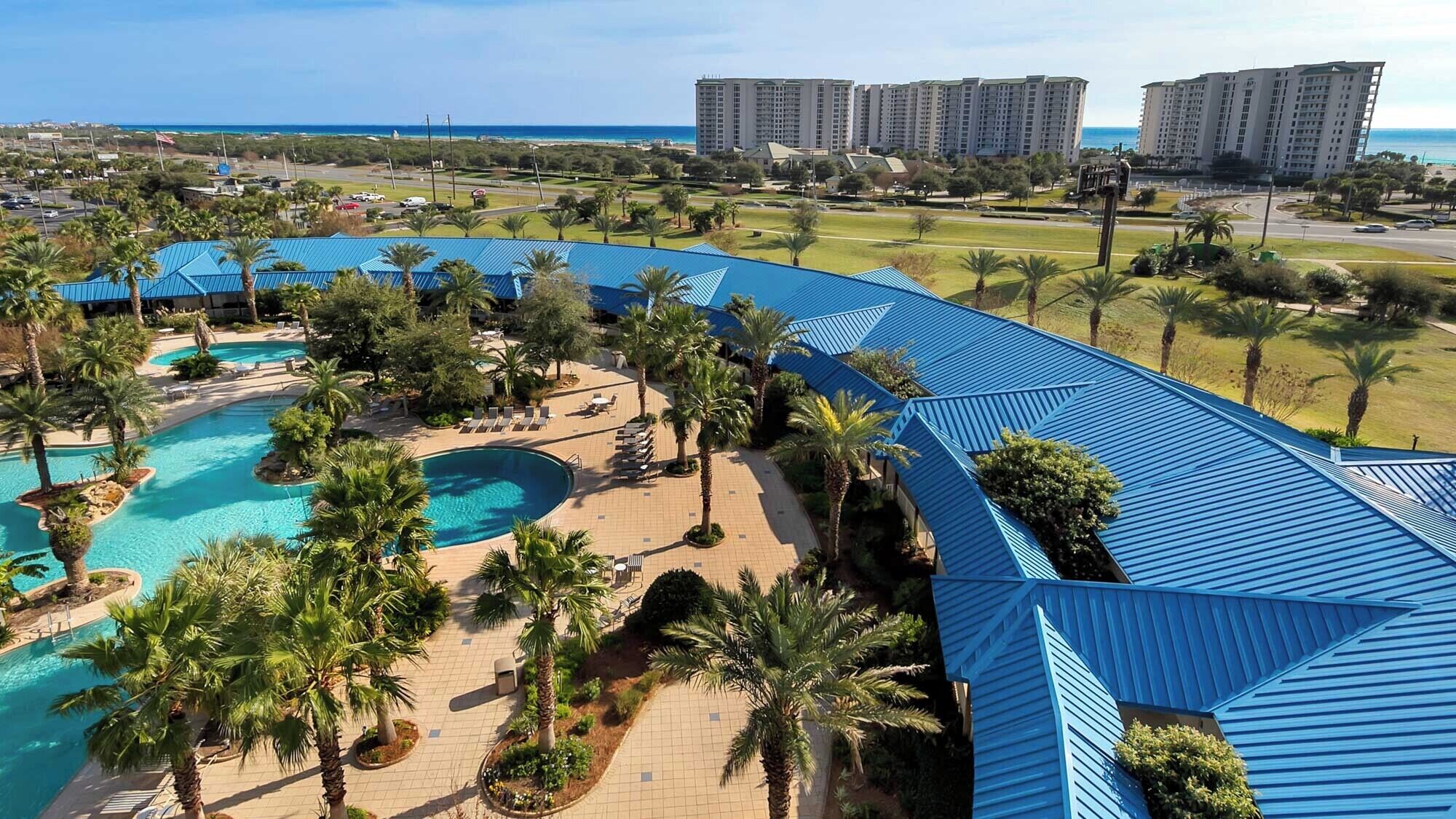 Un resort con una piscina grande, palmeras y vista al océano.
