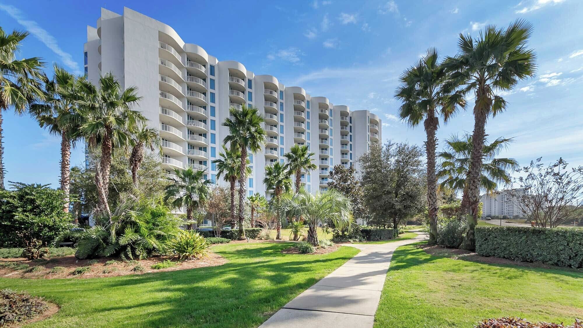 Un hotel moderno de varios pisos, rodeado de exuberante vegetación y palmeras.