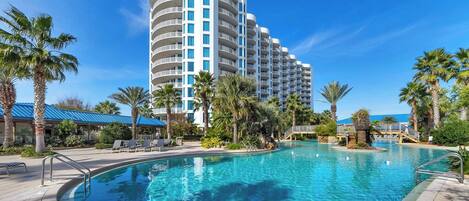 A hotel with a large pool, palm trees, and a clear blue sky.