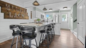 Una cocina moderna con una isla central, taburetes de bar y un letrero de madera en la pared.